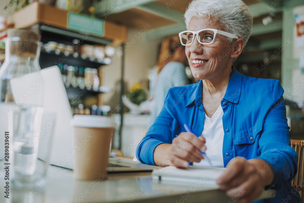Fototapeta premium Positive lady making notes in cafe stock photo