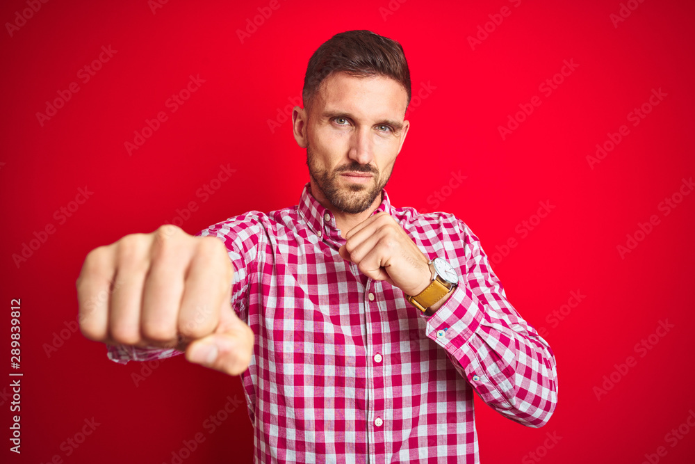 Young handsome man over red isolated background Punching fist to fight, aggressive and angry attack, threat and violence Young handsome man over red isolated background Punching fist to fight, aggressive and angry attack, threat and violence