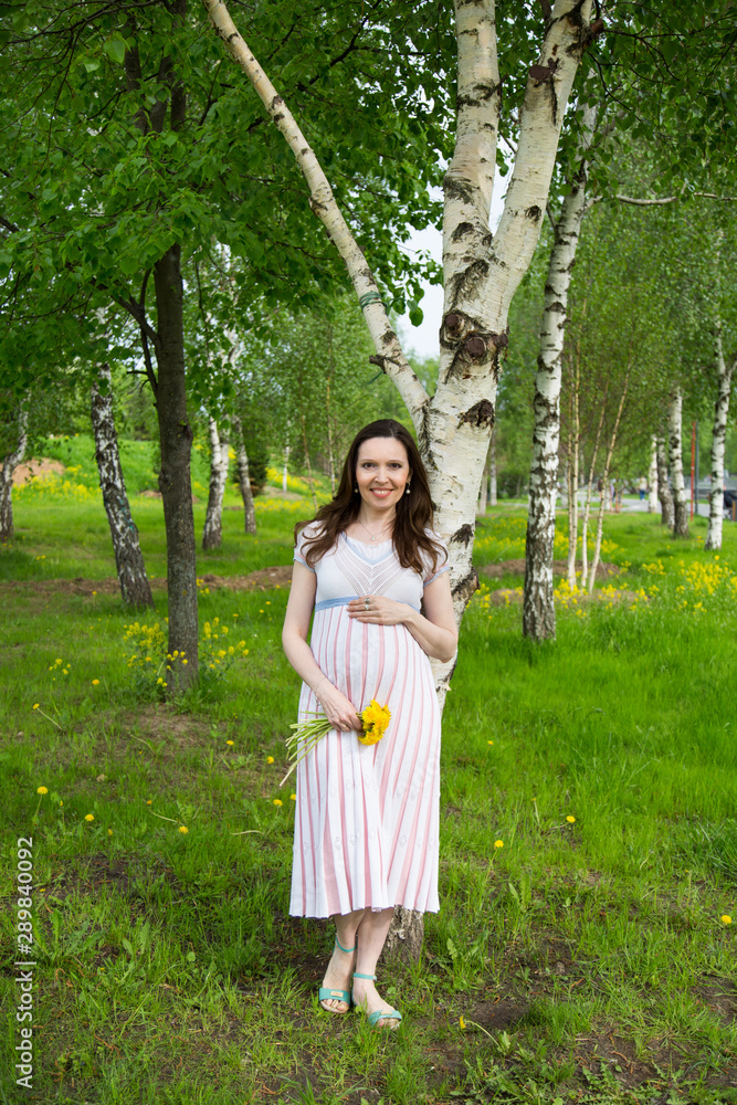 pregnancy, motherhood, the concept of waiting-close - up of a happy pregnant woman with a big belly with a bouquet of flowers at the birch. pregnancy, motherhood, the concept of waiting-close - up of a happy pregnant woman with a big belly with a bouquet of flowers at the birch.
