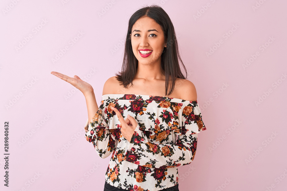 Young chinese woman wearing floral t-shirt standing over isolated pink background amazed and smiling to the camera while presenting with hand and pointing with finger. Young chinese woman wearing floral t-shirt standing over isolated pink background amazed and smiling to the camera while presenting with hand and pointing with finger.
