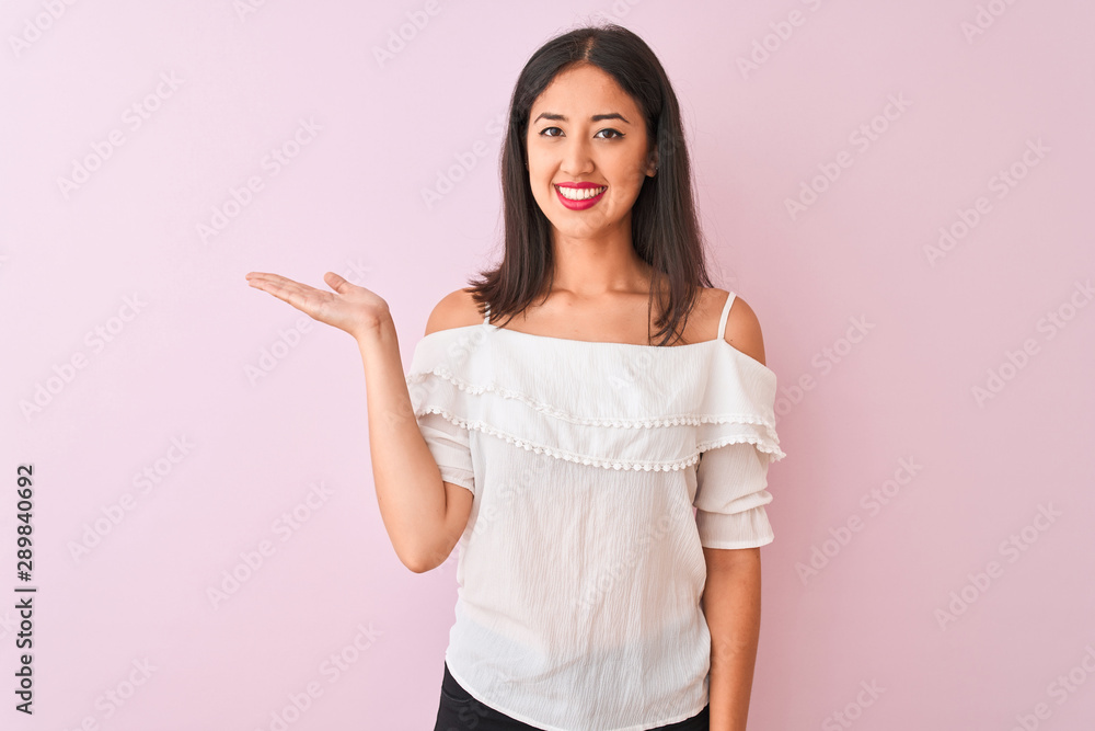 Beautiful chinese woman wearing white t-shirt standing over isolated pink background smiling cheerful presenting and pointing with palm of hand looking at the camera. Beautiful chinese woman wearing white t-shirt standing over isolated pink background smiling cheerful presenting and pointing with palm of hand looking at the camera.