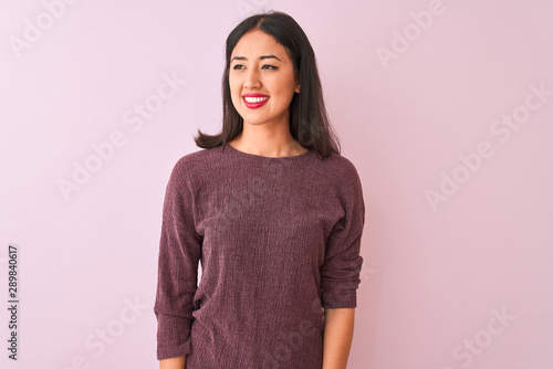 Young chinese woman wearing purple sweater standing over isolated pink background looking away to side with smile on face, natural expression. Laughing confident. © Krakenimages.com