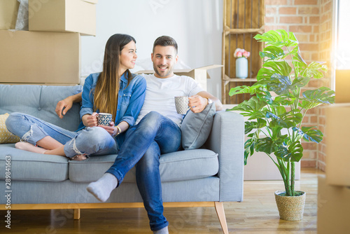 Young couple moving to a new home relaxing sitting on the sofa while drinking a cup of coffee, smiling happy for moving to new apartment