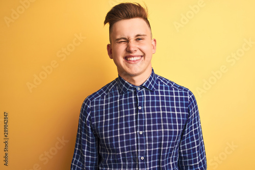Young handsome man wearing casual shirt standing over isolated yellow background winking looking at the camera with sexy expression, cheerful and happy face.