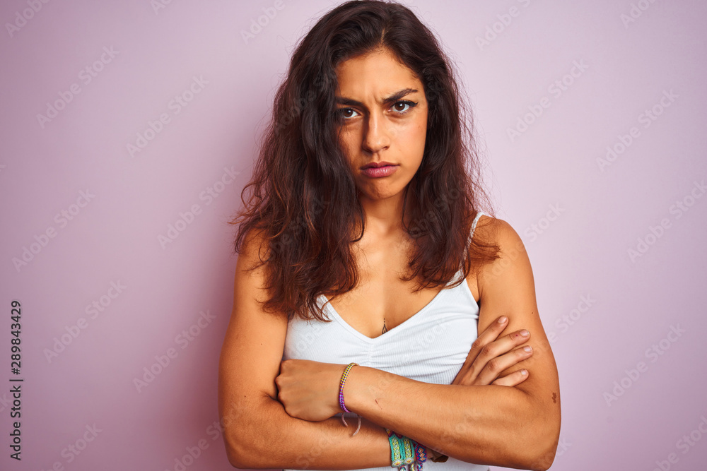 Young beautiful woman wearing white t-shirt standing over isolated pink background skeptic and nervous, disapproving expression on face with crossed arms. Negative person. Young beautiful woman wearing white t-shirt standing over isolated pink background skeptic and nervous, disapproving expression on face with crossed arms. Negative person.