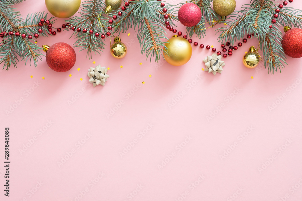 Christmas holiday composition. Christmas tree fir branches, colorful balls on top border on pastel pink background with copy space. Banner mockup, postcard template. Flat lay, top view, overhead.