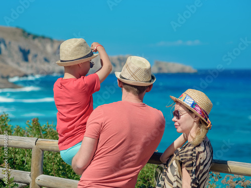 European boy and his parents standing on mountain beyond wonderful blue sea. They  having best holidays ever on the amazing seacost.
