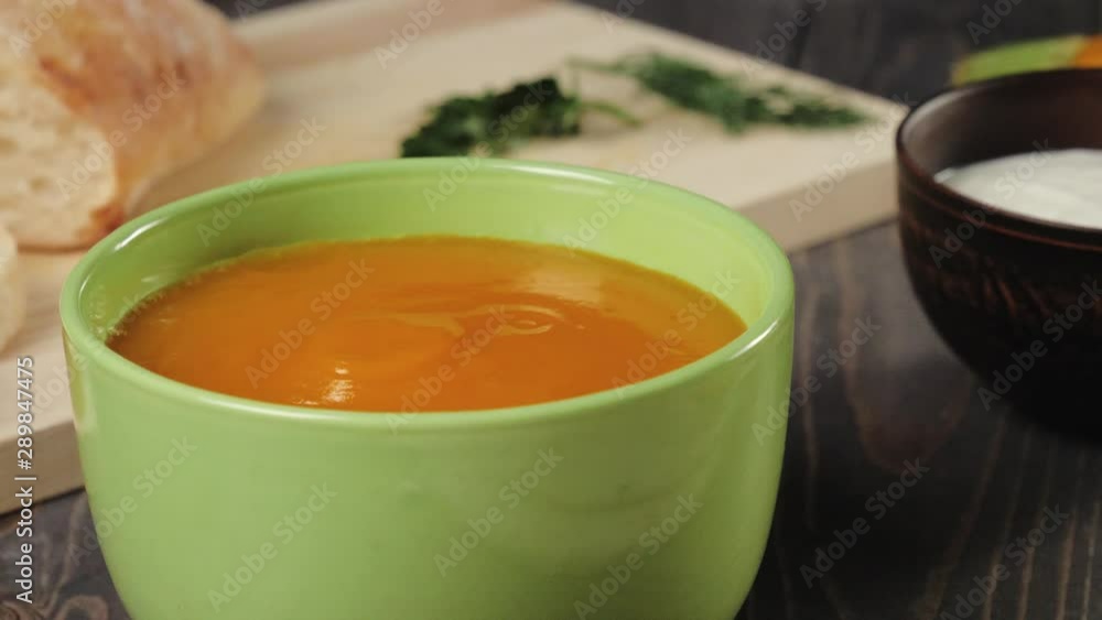 Creamy pumpkin soup cooking. Chef puts creamy pumpkin soup in a green bowl on decorated wooden table. Close up. 4K. Creamy pumpkin soup cooking. Chef puts creamy pumpkin soup in a green bowl on decorated wooden table. Close up. 4K.