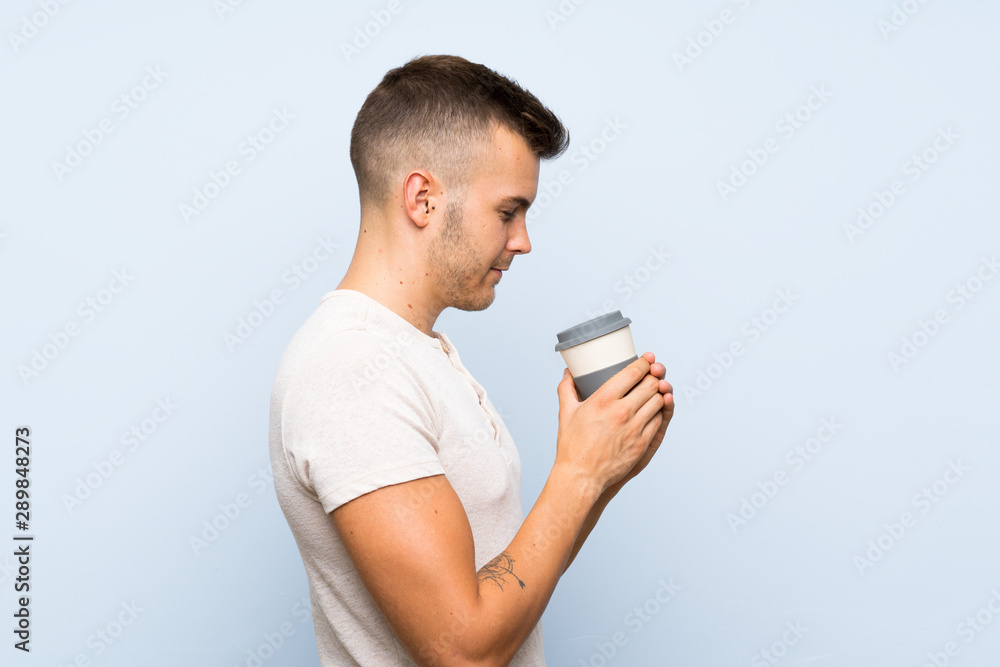 Young handsome blonde man over isolated blue background holding hot cup of coffee Young handsome blonde man over isolated blue background holding hot cup of coffee