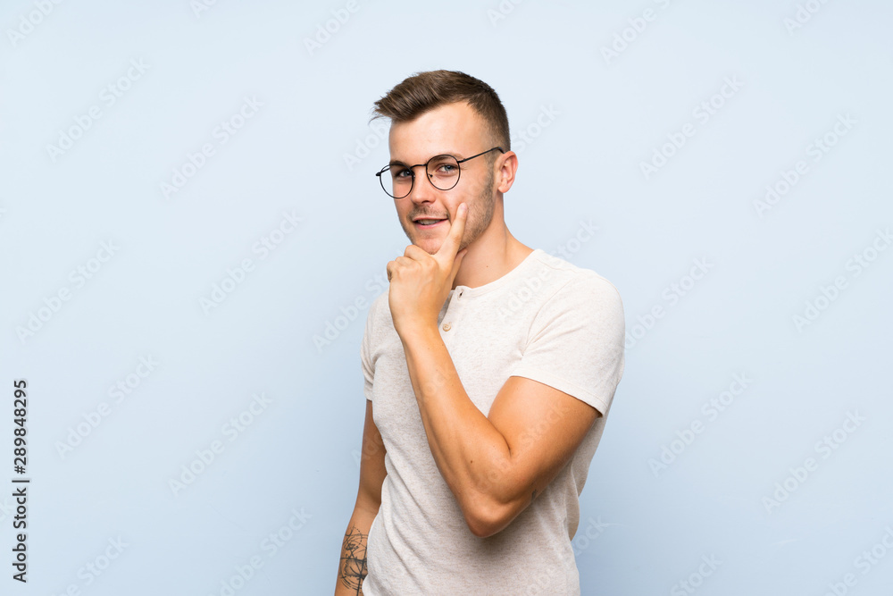 Young handsome blonde man over isolated blue background with glasses Young handsome blonde man over isolated blue background with glasses