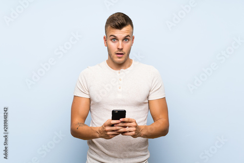 Young handsome blonde man over isolated blue background using mobile phone © luismolinero