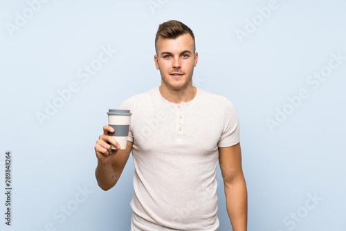 Young handsome blonde man over isolated blue background holding hot cup of coffee