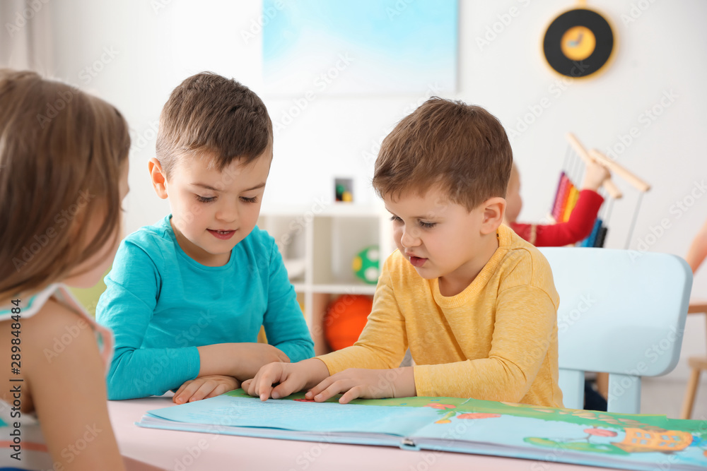 Cute little children reading book together at table indoors. Learning and playing Cute little children reading book together at table indoors. Learning and playing