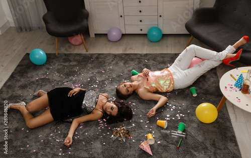 Drunk friends sleeping on floor in messy room after party photo