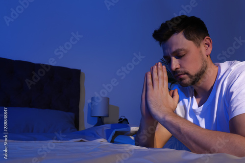 Handsome man saying bedtime prayer in dark room at night. Space for text