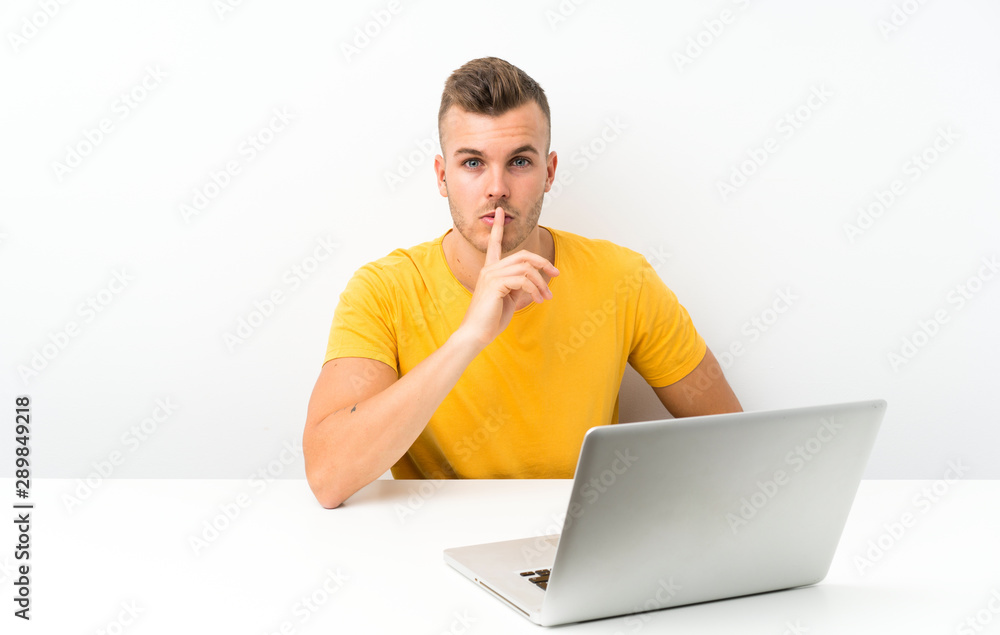 Young blonde man in a table with a laptop doing silence gesture Young blonde man in a table with a laptop doing silence gesture