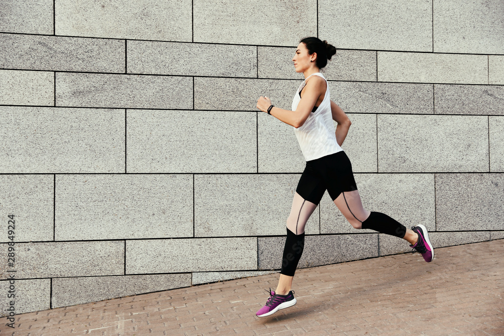 Fototapeta premium Beautiful sporty young woman running on street, space for text