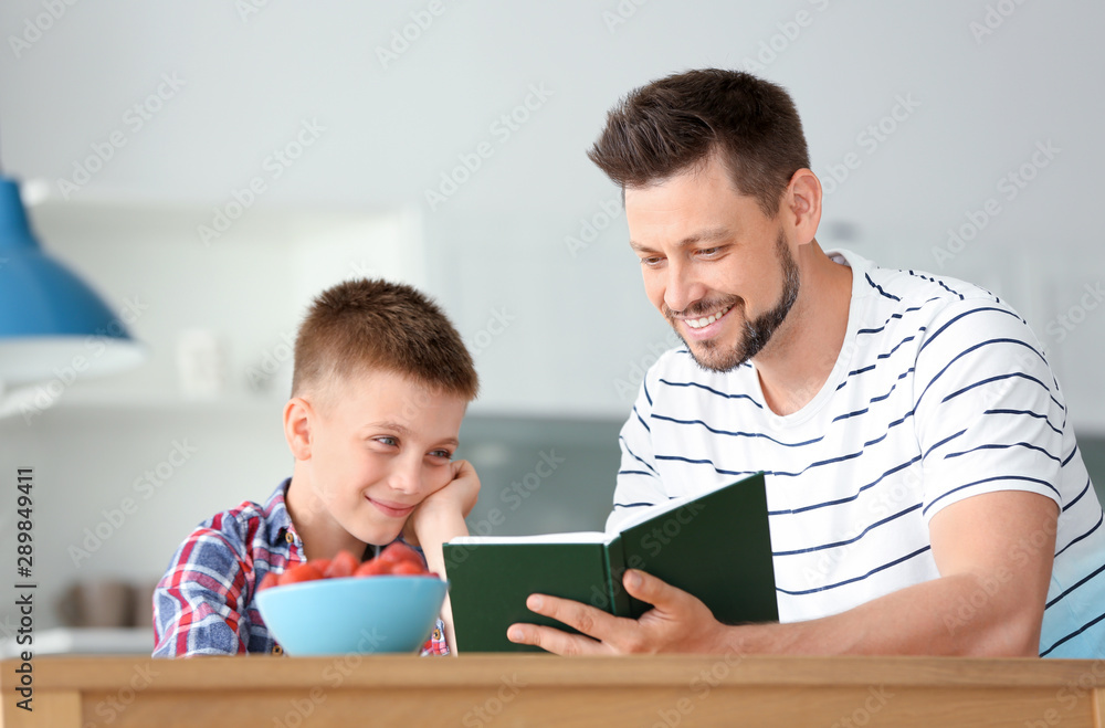 Dad and son reading interesting book in kitchen Dad and son reading interesting book in kitchen