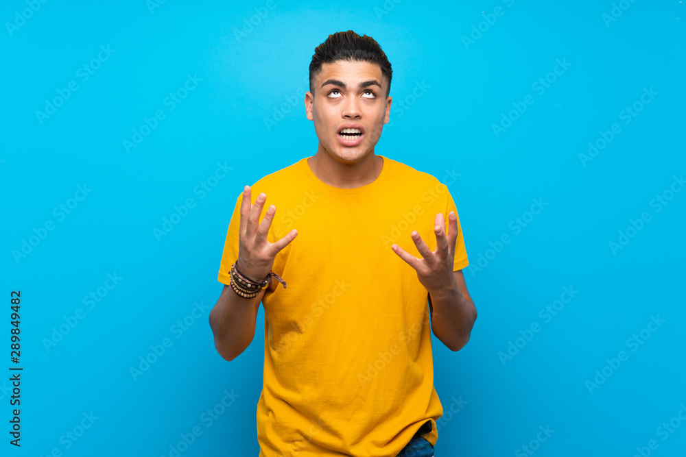 Young man with yellow shirt over isolated blue background frustrated by a bad situation Young man with yellow shirt over isolated blue background frustrated by a bad situation