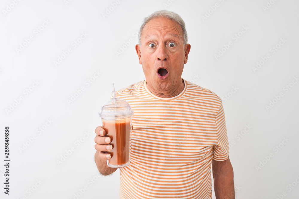 Senior man wearing striped t-shirt drinking tomato smoothie over isolated white background scared in shock with a surprise face, afraid and excited with fear expression Senior man wearing striped t-shirt drinking tomato smoothie over isolated white background scared in shock with a surprise face, afraid and excited with fear expression
