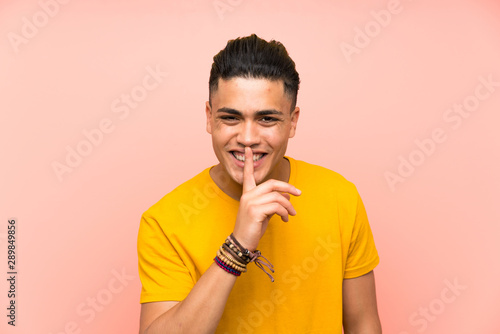 Young man with yellow shirt over isolated pink wall doing silence gesture