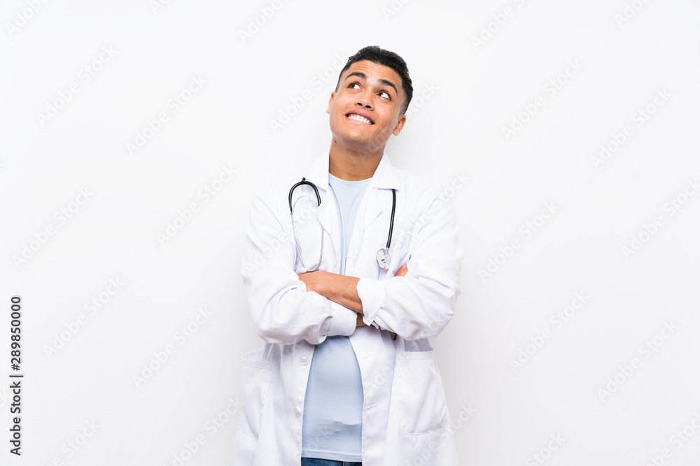 Young doctor man over isolated white wall looking up while smiling Young doctor man over isolated white wall looking up while smiling