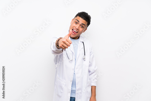 Young doctor man over isolated white wall with thumbs up because something good has happened © luismolinero