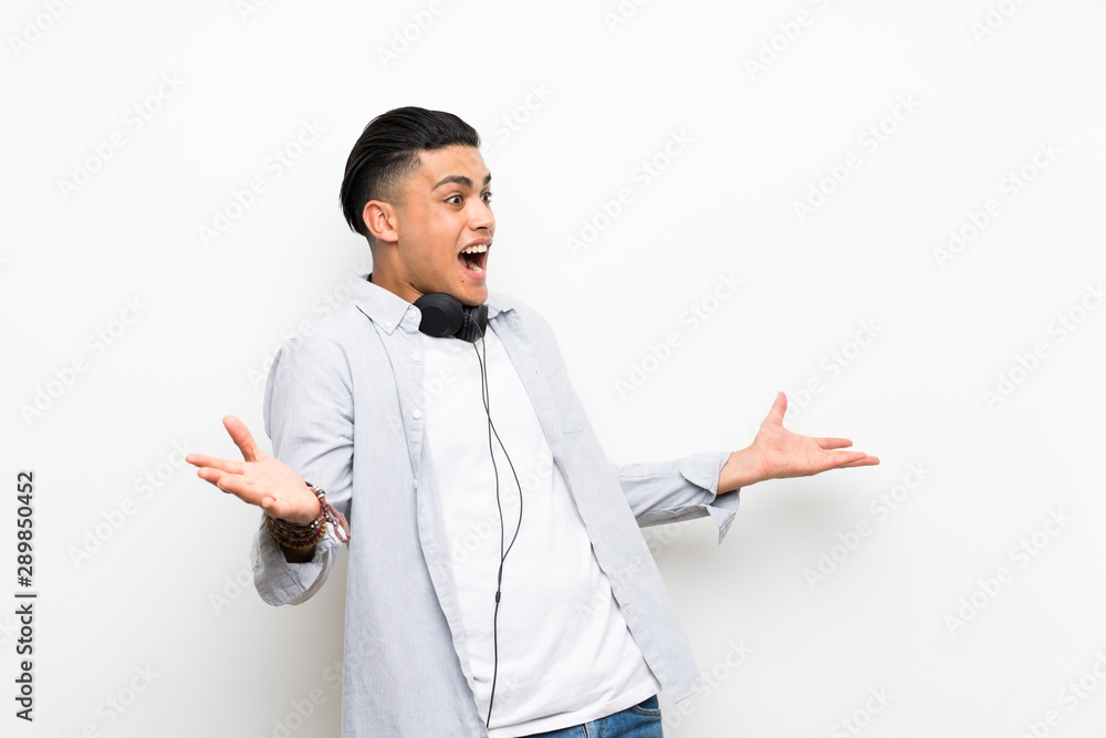 Young man over isolated white wall with earphones with surprise facial expression Young man over isolated white wall with earphones with surprise facial expression