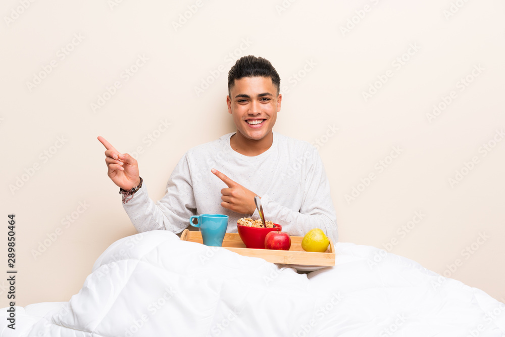 Young man having breakfast in bed pointing finger to the side Young man having breakfast in bed pointing finger to the side