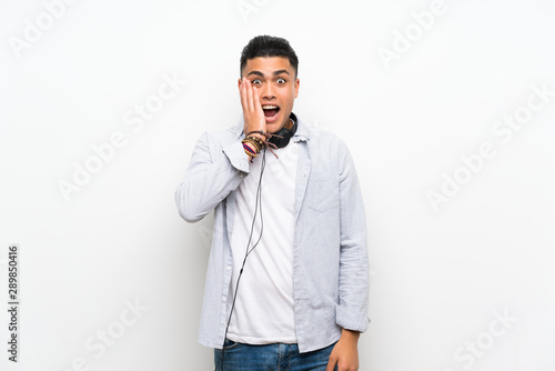 Young man over isolated white wall with earphones with surprise and shocked facial expression