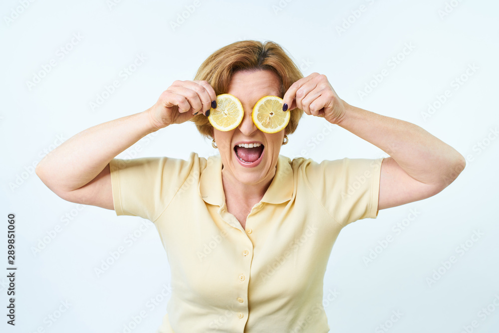 Senior woman with lemon in hand doing funky action. Beautiful woman is covering her eyes with slices of lemon.