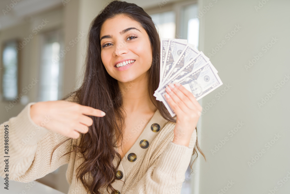 Young woman holding 50 dollars bank notes with surprise face pointing finger to himself Young woman holding 50 dollars bank notes with surprise face pointing finger to himself