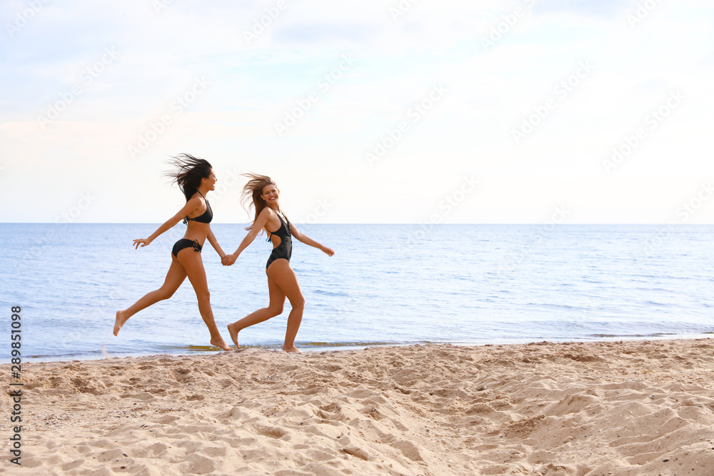 Young woman in bikini with girlfriend on beach. Lovely couple