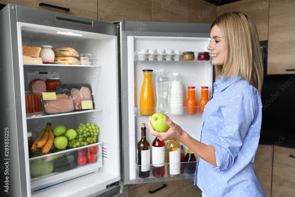 Woman with apple near refrigerator in kitchen Woman with apple near refrigerator in kitchen