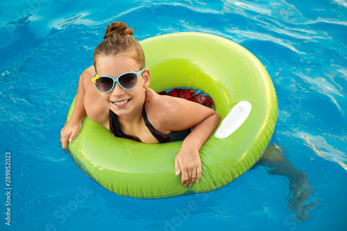 Happy little girl with inflatable ring in swimming pool