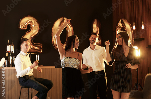 Young people celebrating New Year in club. Golden 2020 balloons on background