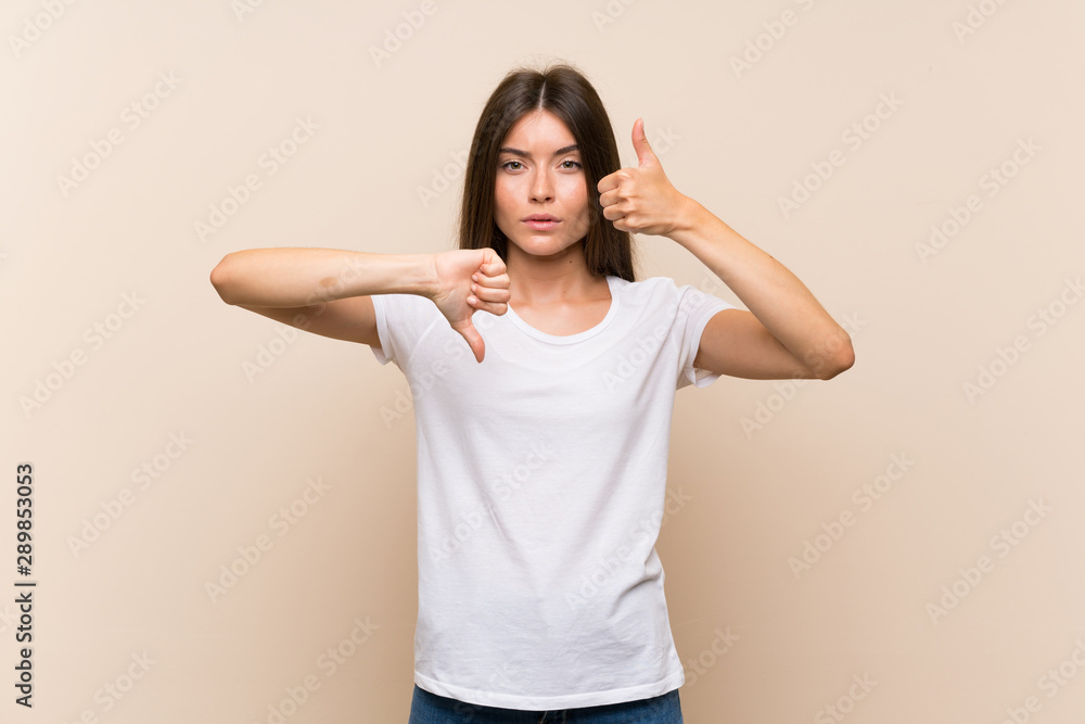 Pretty young girl over isolated background making good-bad sign. Undecided between yes or not Pretty young girl over isolated background making good-bad sign. Undecided between yes or not