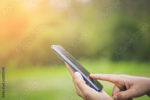 Woman hand using smart phone at outdoor nature park with sunset sky abstract background.