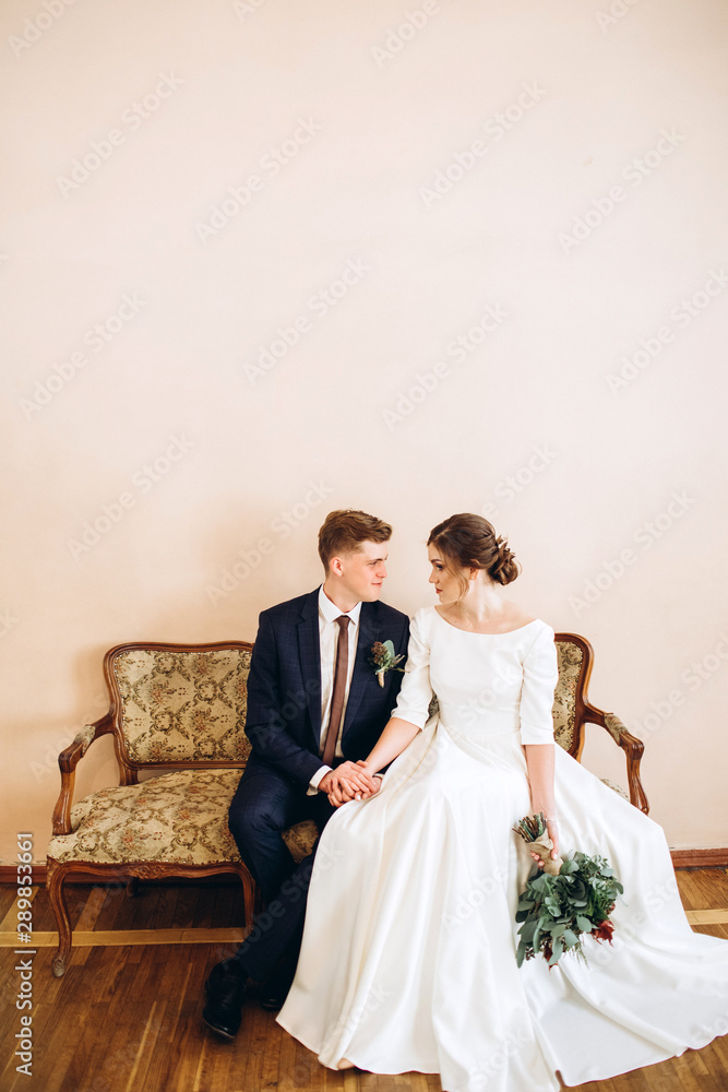 A young couple in wedding dresses in an old mansion. Bride and groom at a wedding ceremony indoors. Loving couple. Emotions. Happy husband and wife. The bride with an autumn bouquet in her hands.