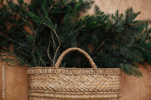 Rustic basket with fir branches on rustic wooden background. Flat lay. Winter holiday preparations. Slow living. Seasons greeting.
