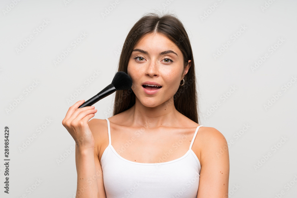 Pretty young woman with makeup brush over isolated grey background Pretty young woman with makeup brush over isolated grey background