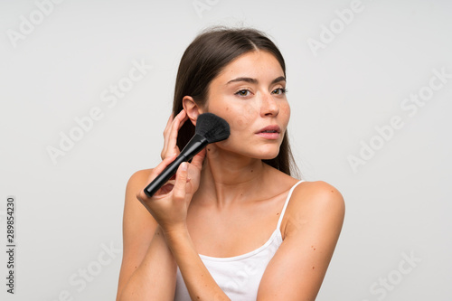 Pretty young woman with makeup brush over isolated grey background