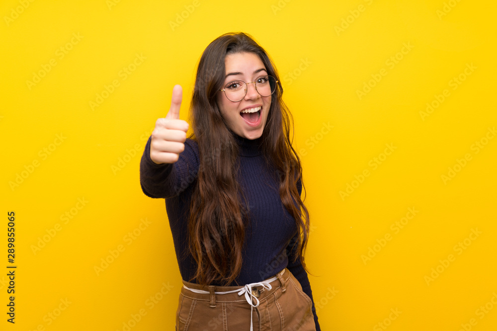 Teenager girl over isolated yellow wall with thumbs up because something good has happened Teenager girl over isolated yellow wall with thumbs up because something good has happened