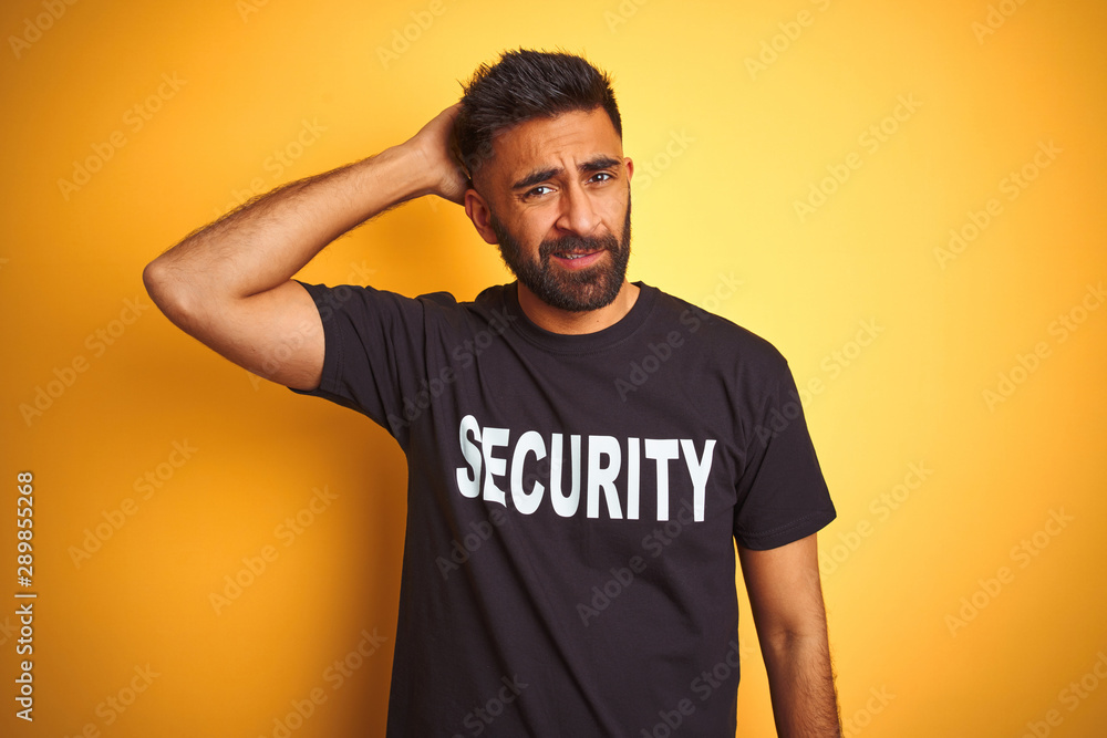 Arab indian hispanic safeguard man wearing security uniform over isolated yellow background confuse and wonder about question. Uncertain with doubt, thinking with hand on head. Pensive concept. Arab indian hispanic safeguard man wearing security uniform over isolated yellow background confuse and wonder about question. Uncertain with doubt, thinking with hand on head. Pensive concept.