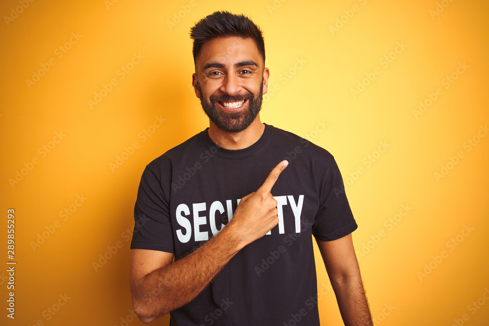 Arab indian hispanic safeguard man wearing security uniform over isolated yellow background cheerful with a smile of face pointing with hand and finger up to the side with happy and natural expression Arab indian hispanic safeguard man wearing security uniform over isolated yellow background cheerful with a smile of face pointing with hand and finger up to the side with happy and natural expression