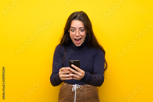 Canvas-taulu Teenager girl over isolated yellow wall surprised and sending a message