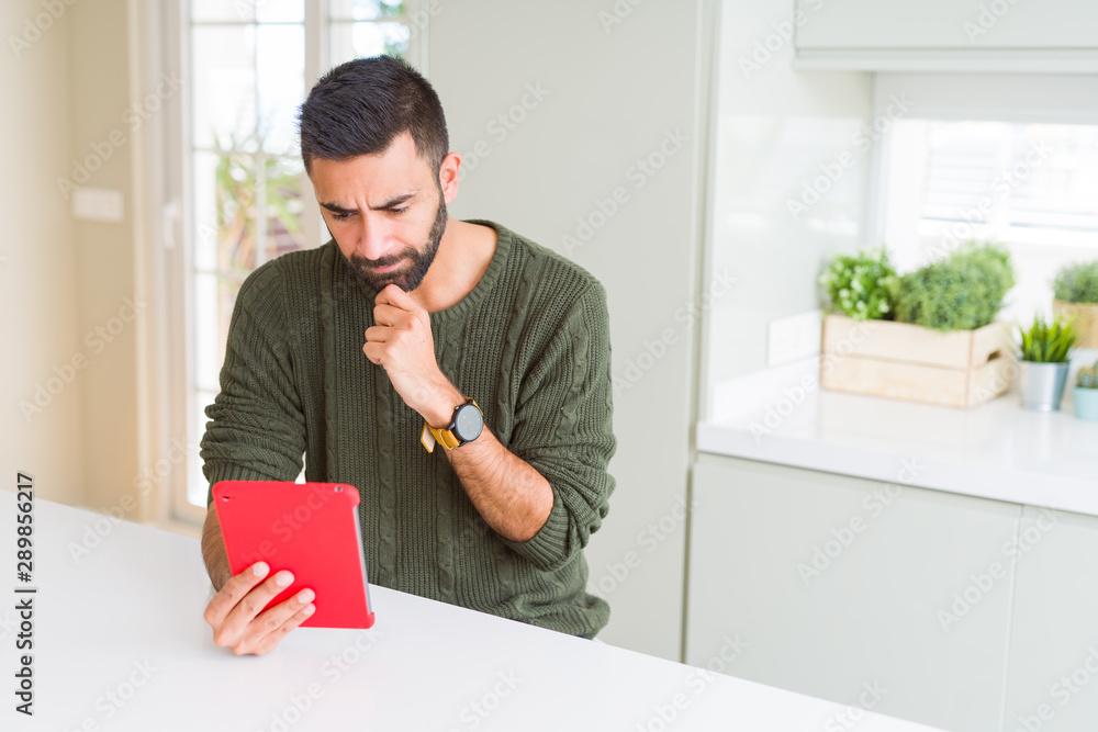 Handsome hispanic man using tablet at home serious face thinking about question, very confused idea