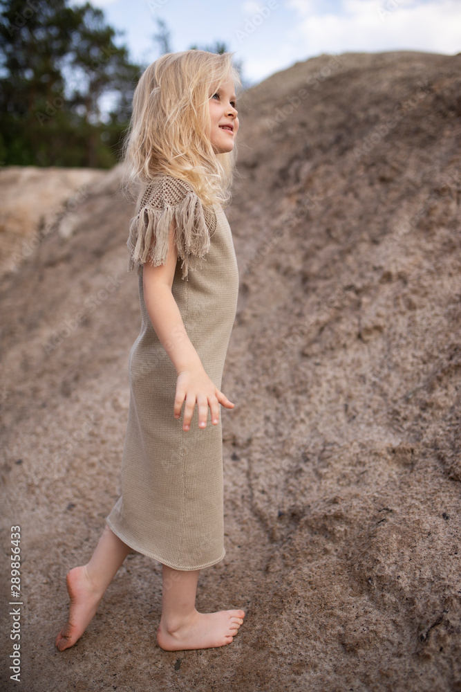 Little cute girl in stylish clothes on a background of rocks. Summer portrait of a little girl in a hat and cotton clothes for a magazine or advertisement Little cute girl in stylish clothes on a background of rocks. Summer portrait of a little girl in a hat and cotton clothes for a magazine or advertisement