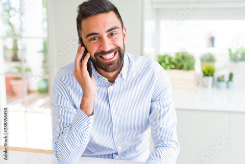 Handsome hispanic business man having a conversation talking on smartphone with a happy face standing and smiling with a confident smile showing teeth