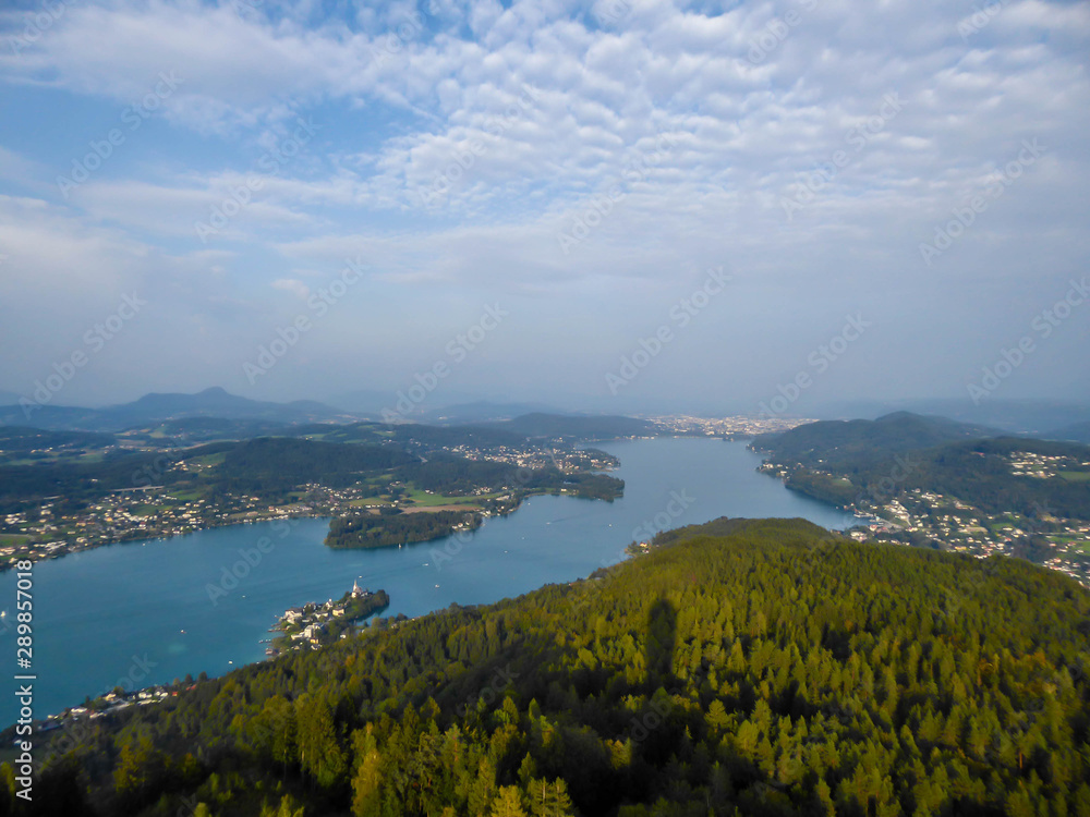 A view on the Wörthersee lake from the observation deck of Pyramidenkogel Tower. Lake is reflecting the last beams of sun for this day. Golden hour. The surrounding hills are shining gold.